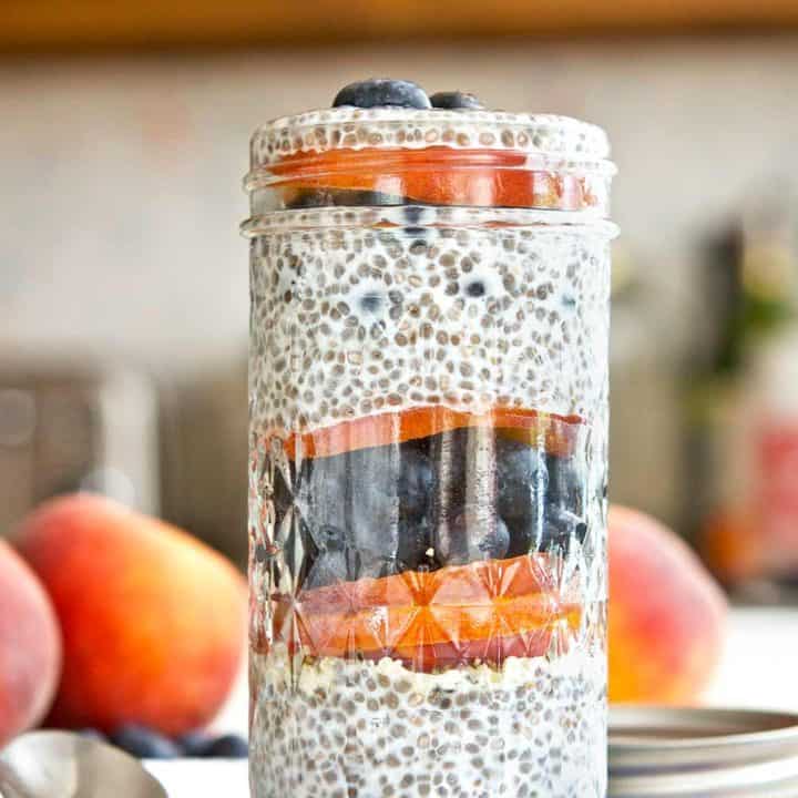 Blueberry peach chia parfait in a glass jar on a floral linen