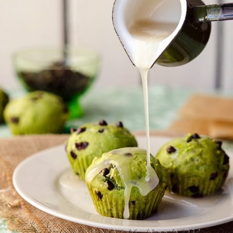 Glaze being poured over green-hued, chocolate chip cupcakes on a white plate