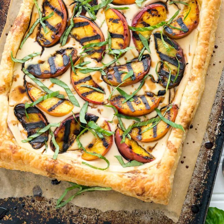 Grilled peaches and cream pastry on a baking sheet next to peaches and linen