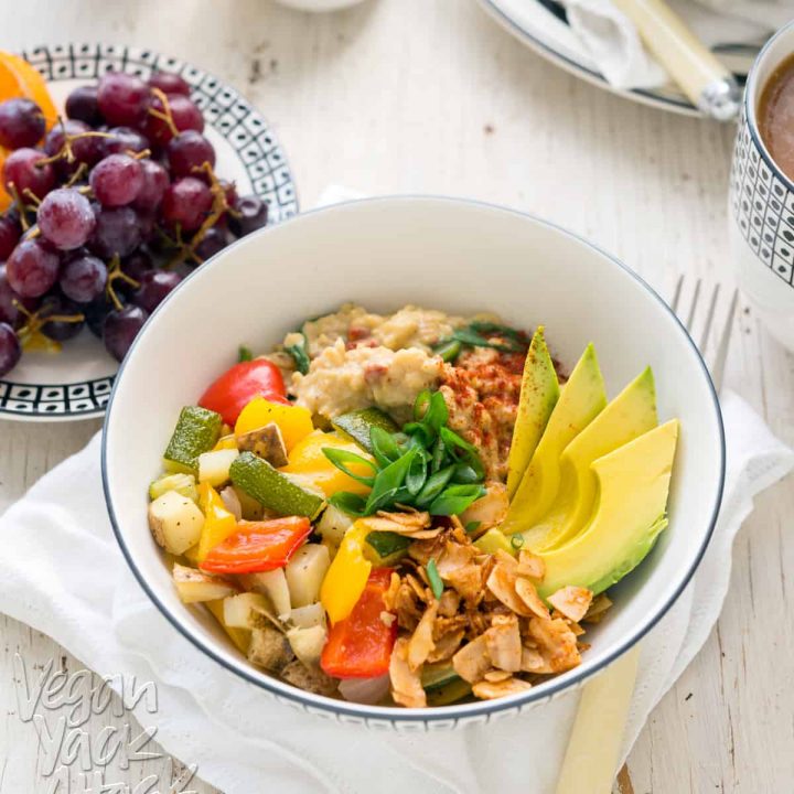 Image of bowl of savory oats with veggies, coconut bacon, and avocado, on a white table top