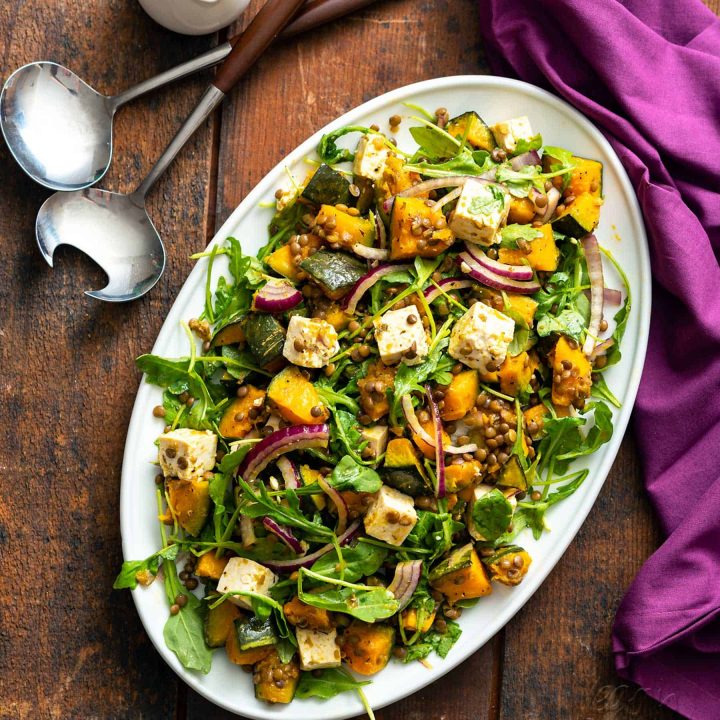 Oval plate filled with kabocha squash salad with vegan feta and lentils, on a wood table