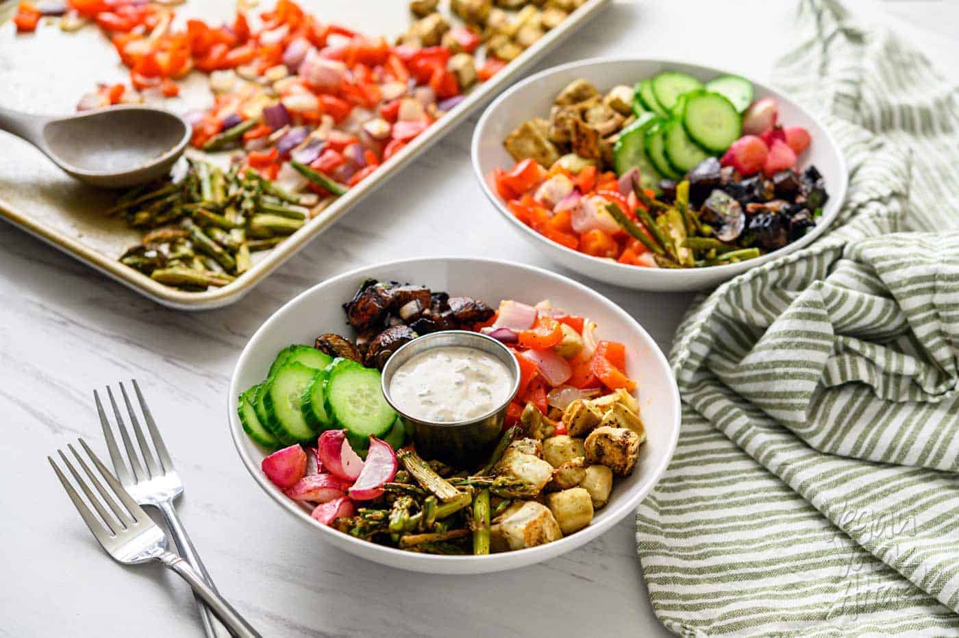 Image of two bowls, filled with a Mediterranean Sheet Pan Meal, and sauce, next to a sheet pan, with text overlay