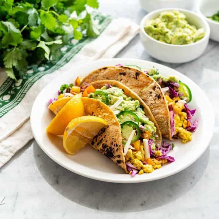 An image of vegan breakfast tacos plated, on a marble table with assorted toppings near it