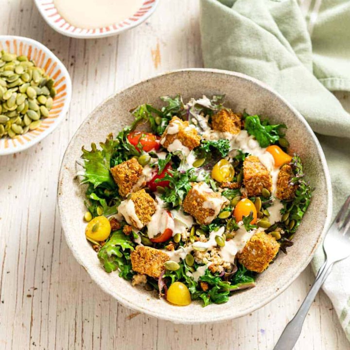 Comforting Tempeh Kale Salad in a ceramic bowl next to a green linen and fork