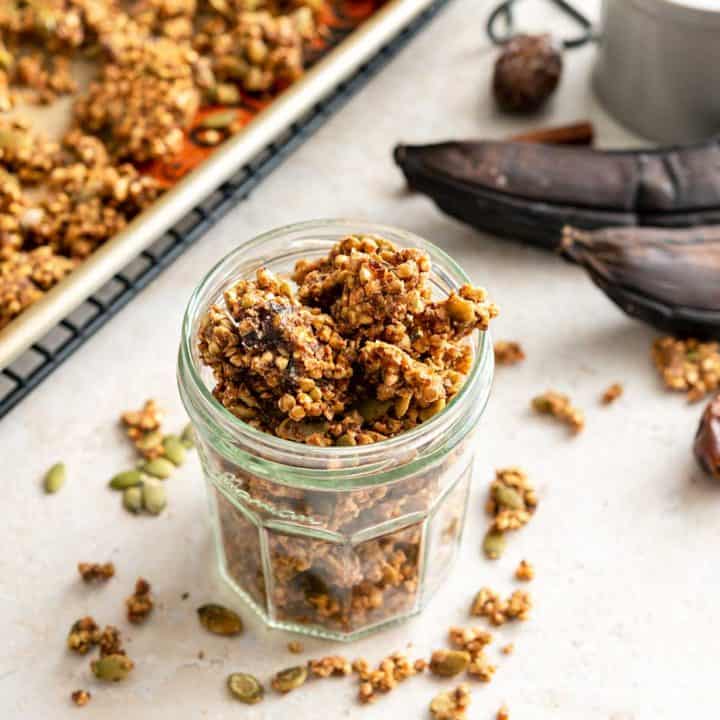 Jar of buckwheat granola next to ripe bananas and baking sheet