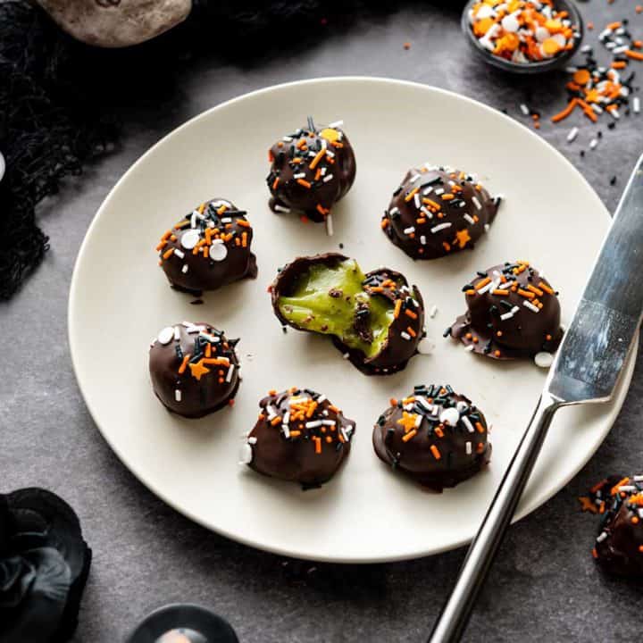 Small light grey plate of truffles with green filling on a black marble background
