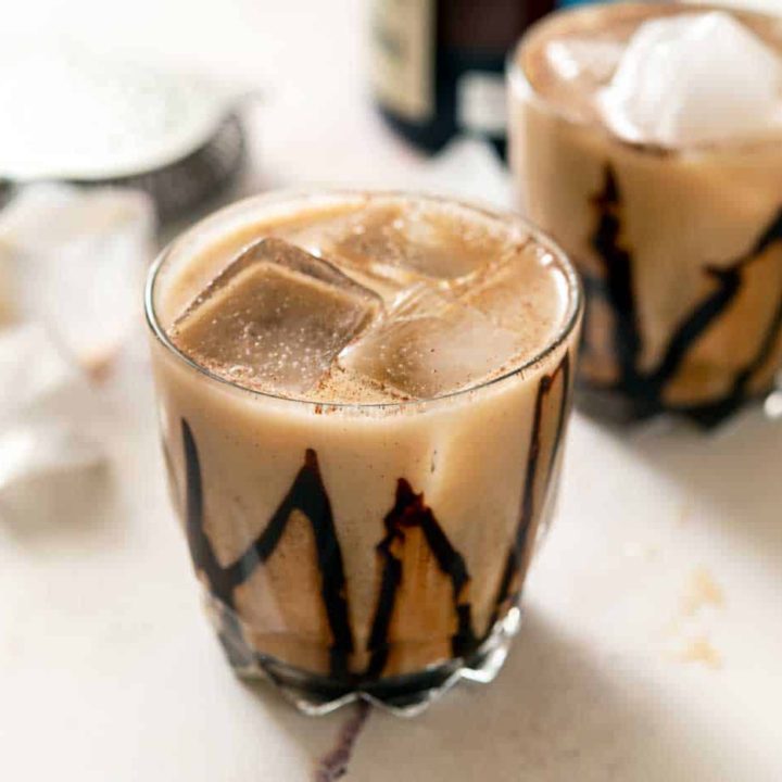 Two glasses with mocha mezcal cocktail over ice, near a bottle of mezcal