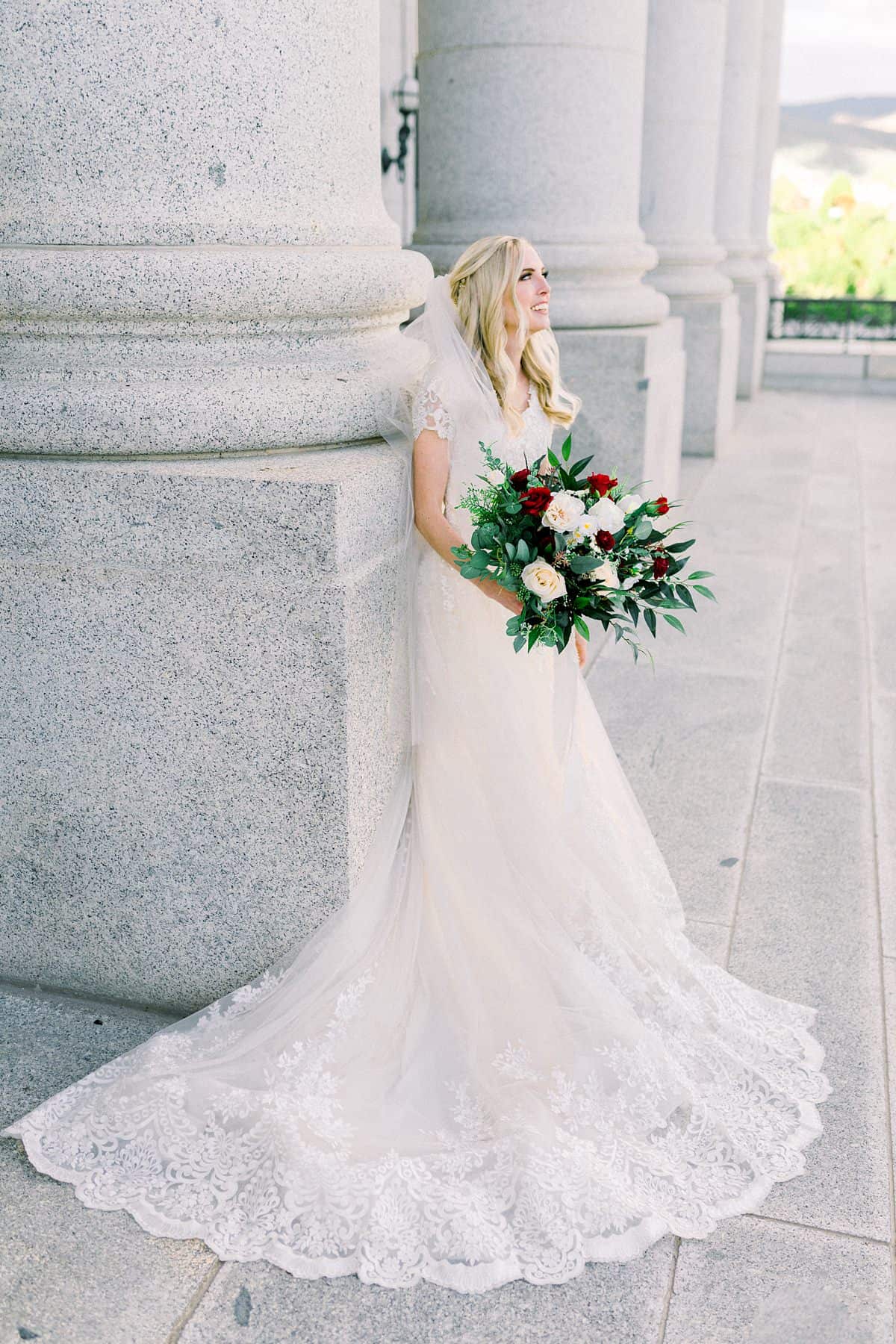 Modest lace wedding dress, bride with long veil and long hairstyle, red and white wedding flowers bouquet