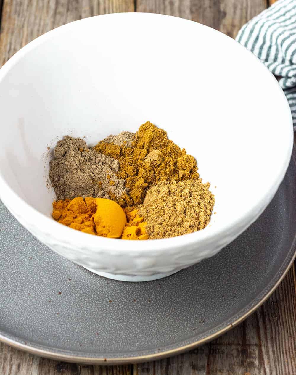 Curry powder ingredients in a white bowl, turmeric, coriander, cardamom and cumin in a white bowl