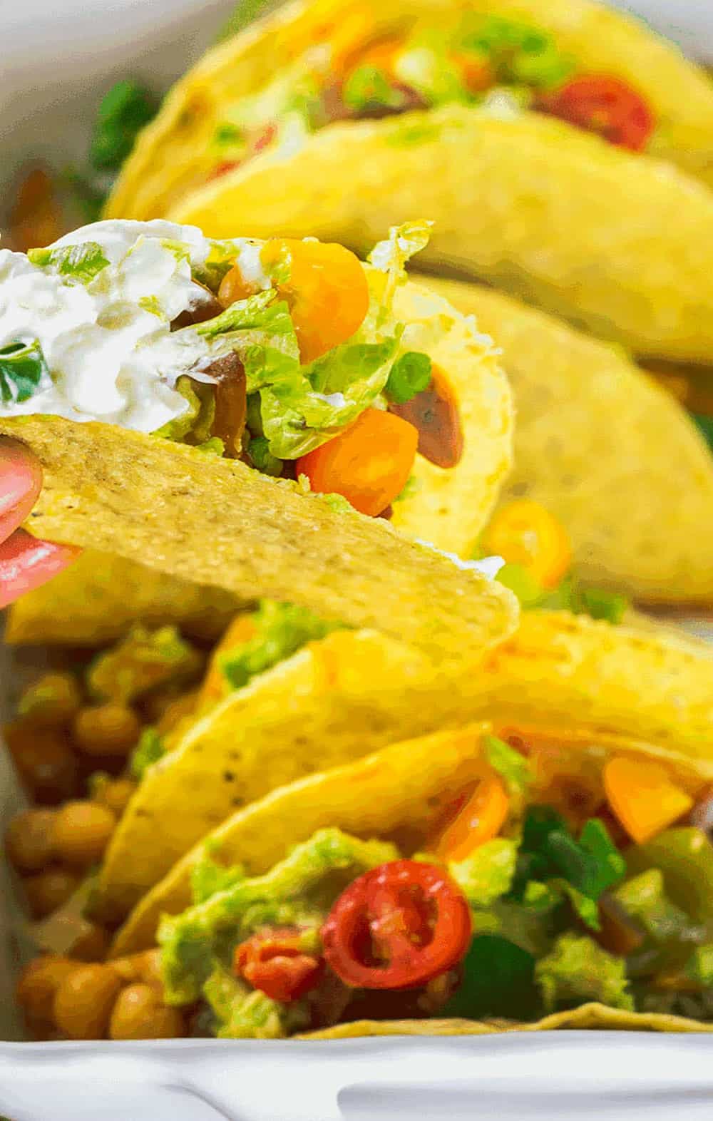 Best Chickpea Tacos with chickpea stew topped with guacamole, tomatoes, sour cream lettuce in a white casserole dish