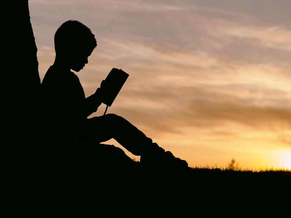 Silhouette of a child reading. Photo by Aaron Burden on Unsplash