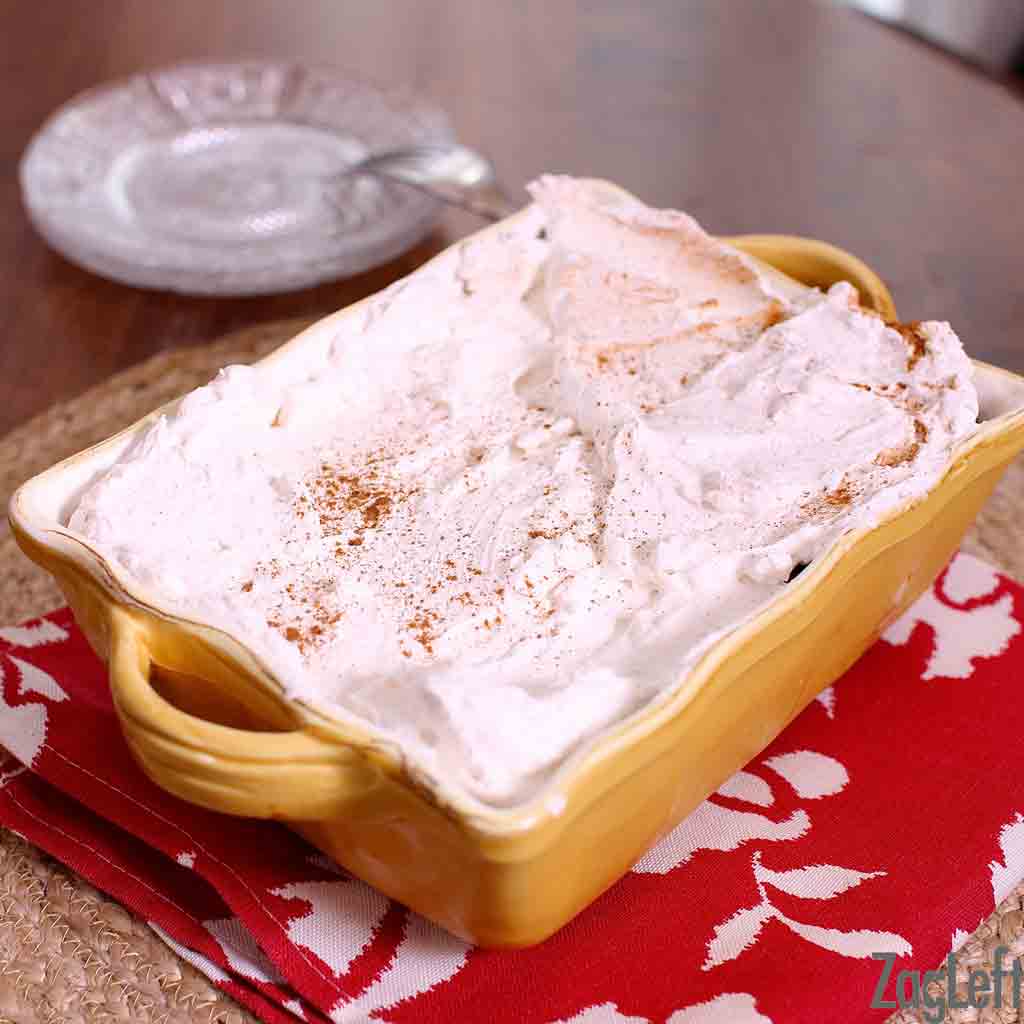 A whole tres leches cake in a small baking dish next to a small stack of plates.