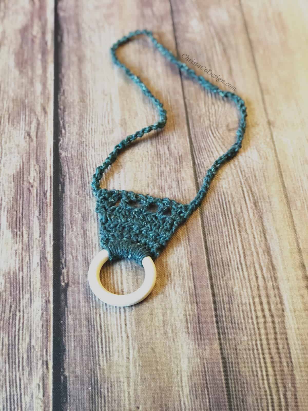picture of easy crochet nursing necklace in dark green yarn with pale maple wood ring as pendant