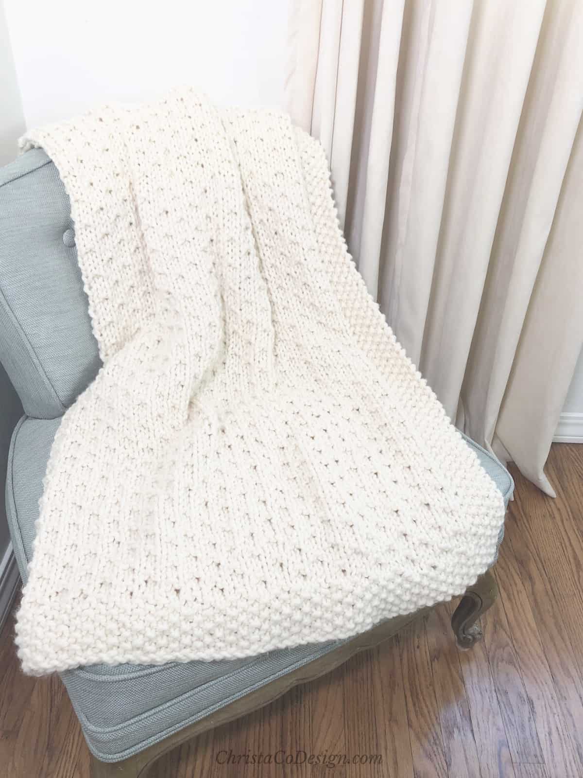 picture of Bella vita easy blanket beginner knitting in cream yarn on blue chair