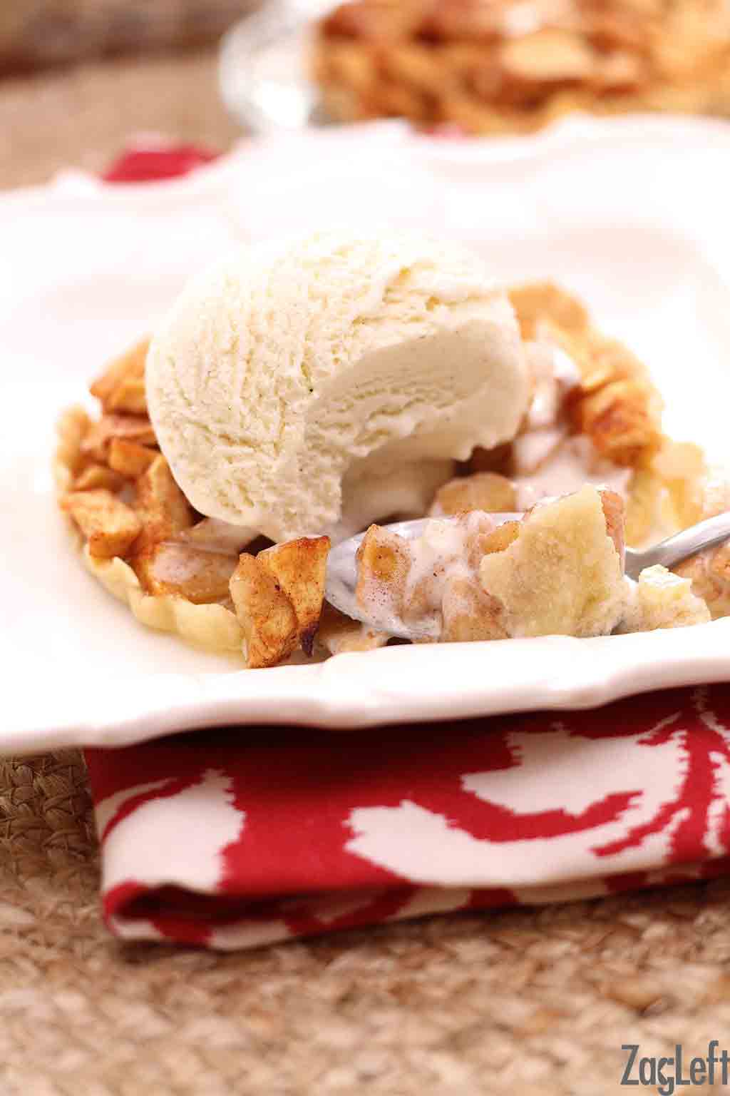 A spoonful of a mini apple pie topped with a scoop of vanilla ice cream