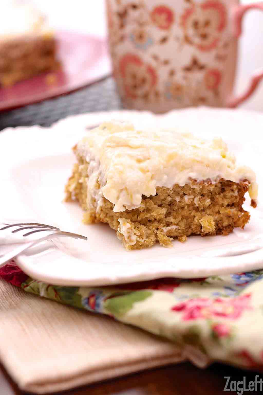 A closeup of a slice of pineapple oat cake next to a coffee mug plated on a floral cloth napkin