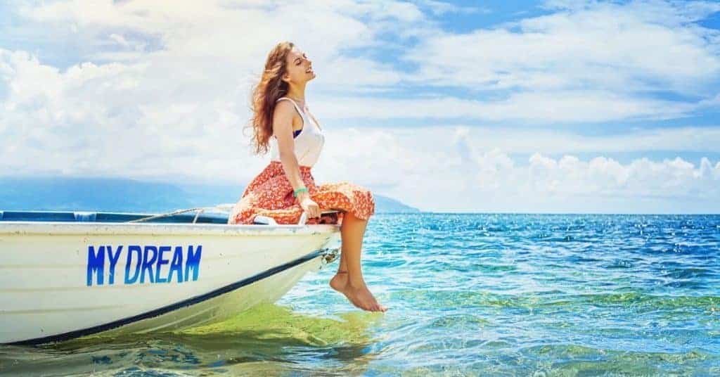 Beautiful woman sitting on edge of a boat named "My Dream" in beautiful blue ocean water - Setting 10-Year goals to live your dream life.