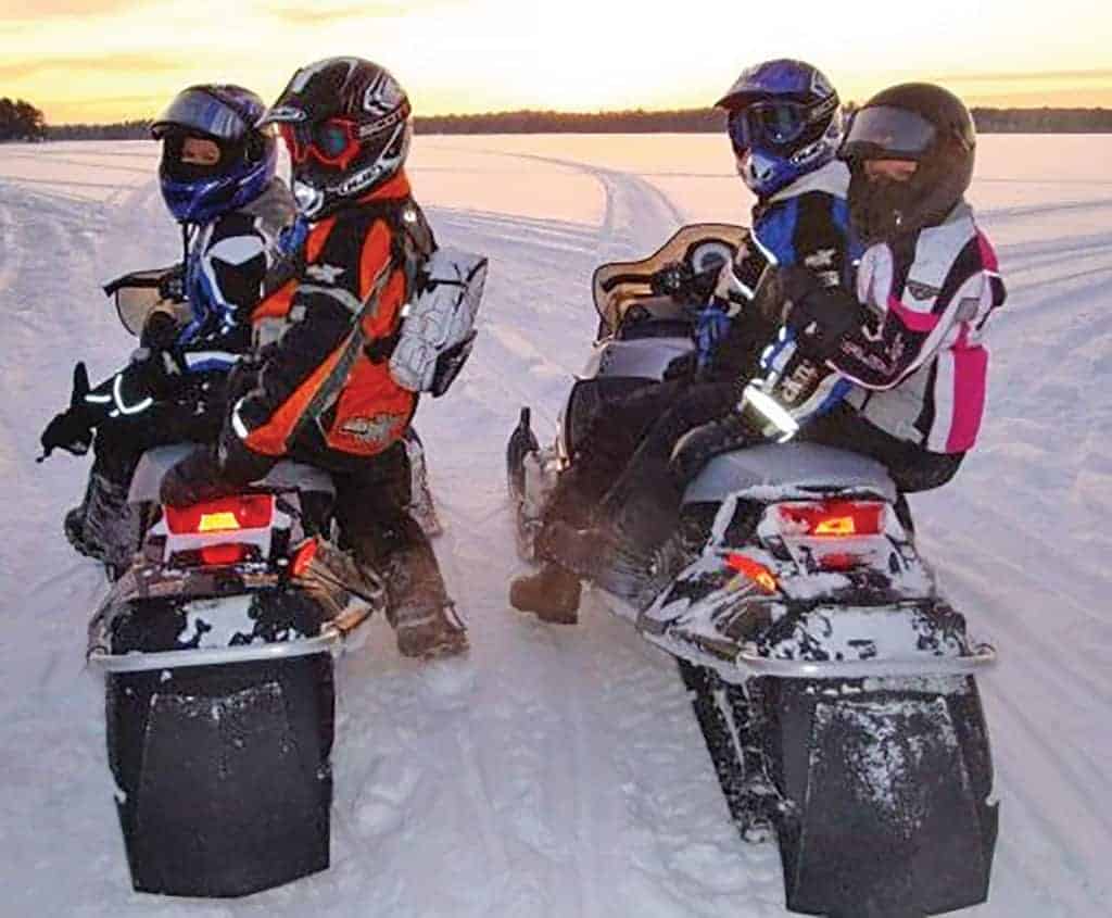 Two couples snowmobiling on a groomed trail.