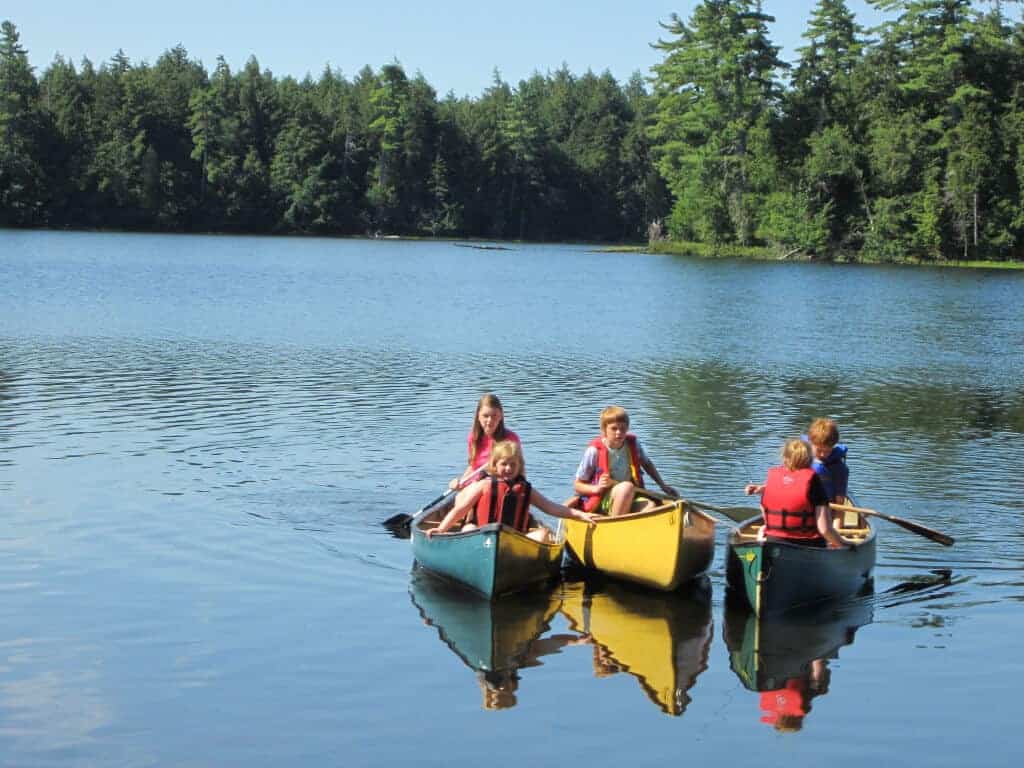 Three canoes side-by-side on a mountain lake in the St. Regis Canoe Area. There are five kids paddling.