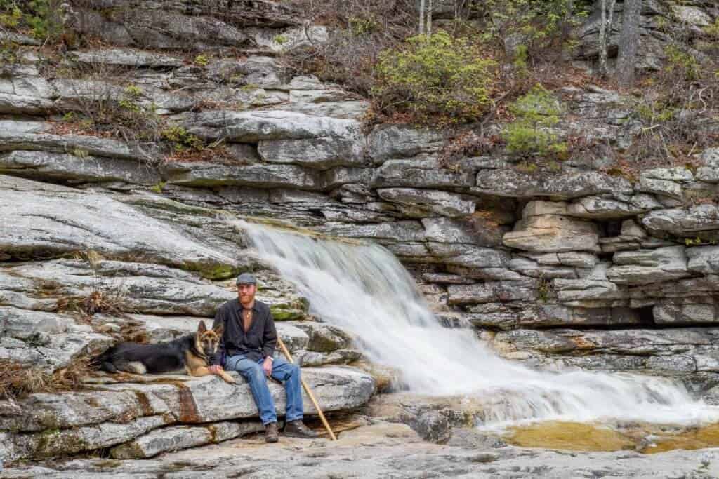 A man and a German Shepherd dog sitting next to a waterfall in the Hudson Valley New York