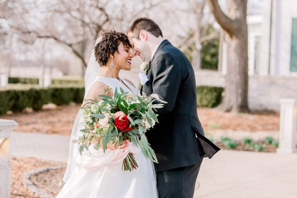 bride and groom standing in the middle of the field touching their foreheads and smiling