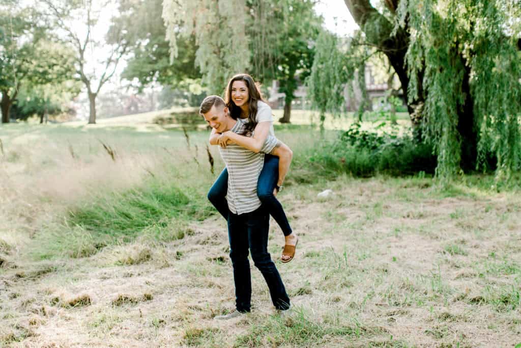 guy holding girl on his back during an engagement session in mayslake peabody estate