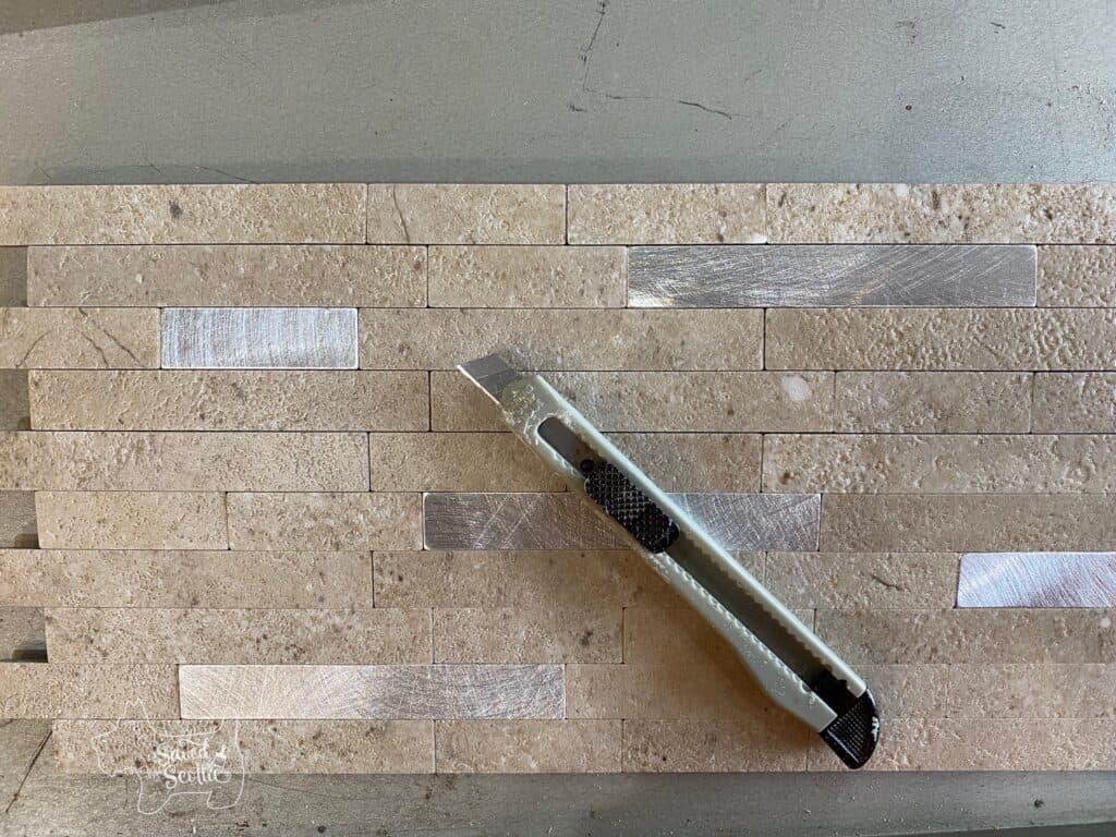 small snap blade utility knife laying on an Aspect Tile stone and metal collage tile.