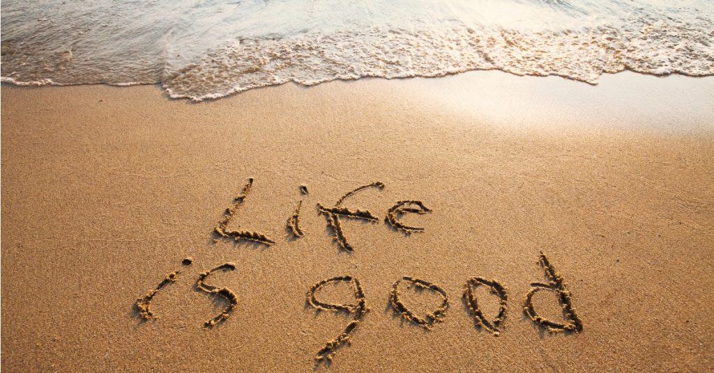 Photo of a beach at sunset with "Life is good" written in the sand.