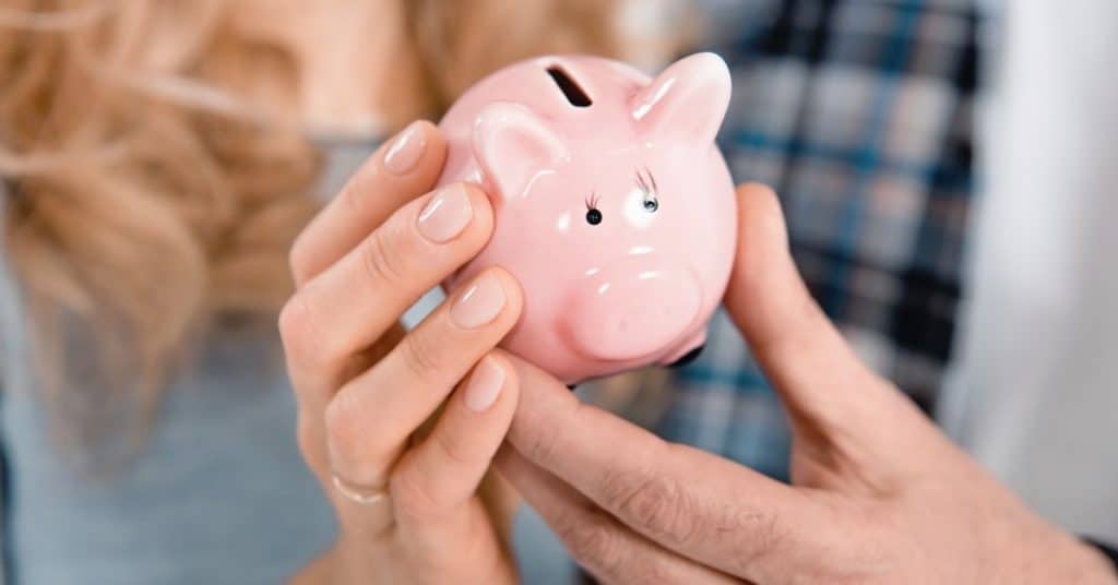close up of a couple holding a small pink piggy bank - marriage and money