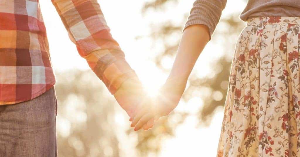 Young couple in love walking in the autumn park holding hands looking in the sunset