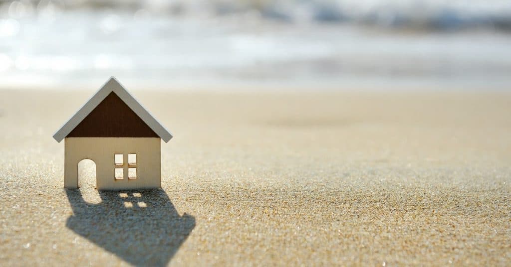 Toy house on the sand with waves in the background - on how to retire early with real estate investing
