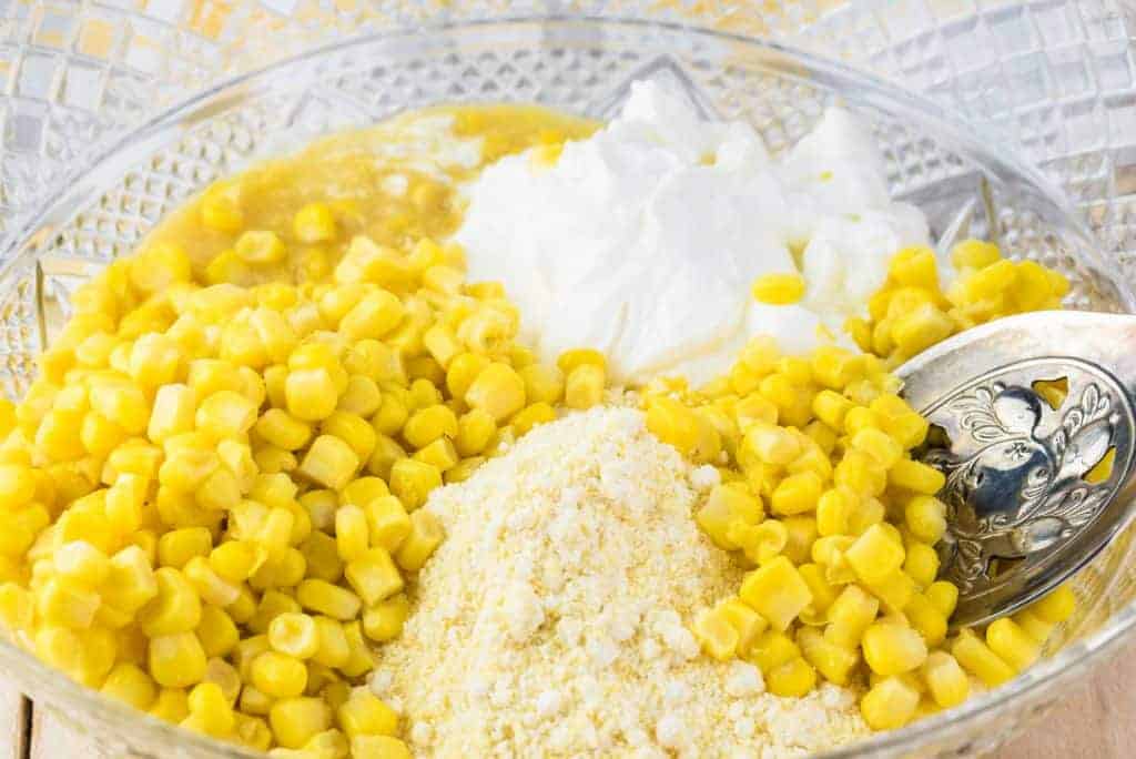 whole corn, creamed corn, corn muffin mix, sour cream, eggs and melted butter in a glass bowl with a spoon