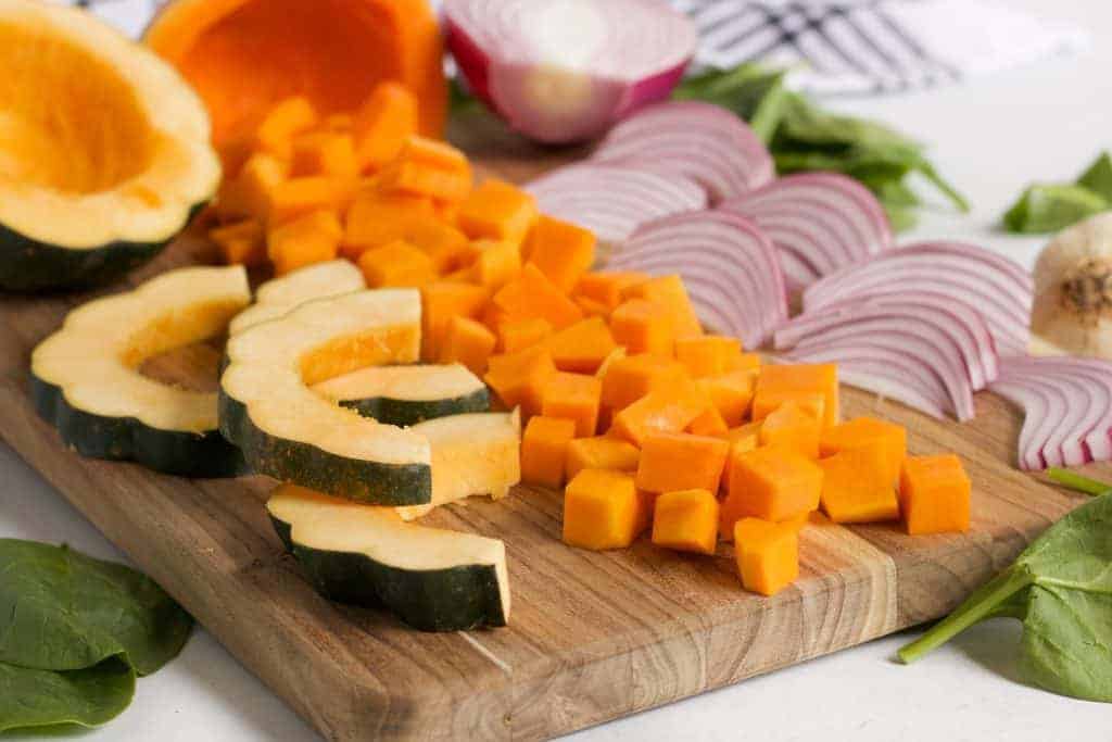 acorn squash, butternut squash and red onions cut on wooden cutting board