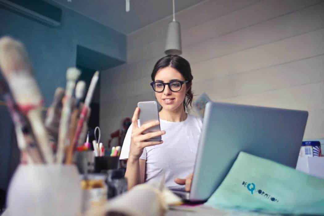 woman smiling while using phone and laptop in an art studio