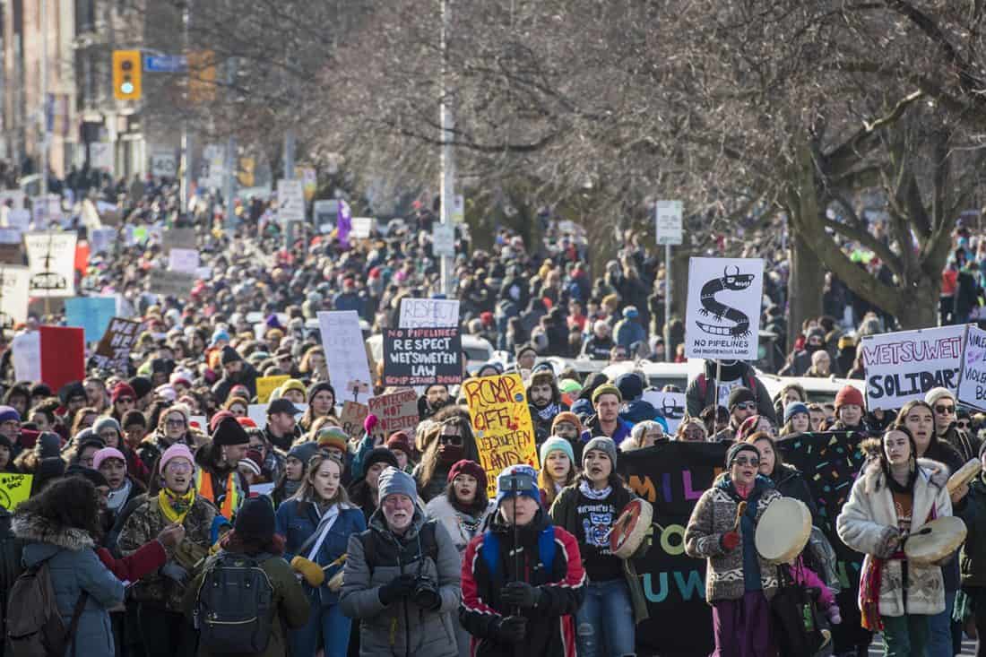 A large crowd bearing signs and drums swarm down an avenue.