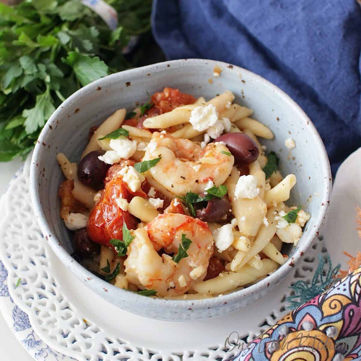 an overhead view of a blue bowl filled with shrimp and pasta and olives.