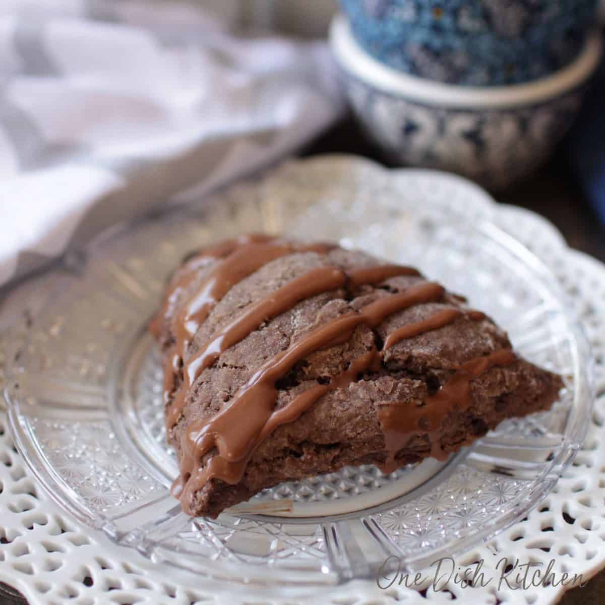 A chocolate scone with chocolate glaze drizzle on a plate