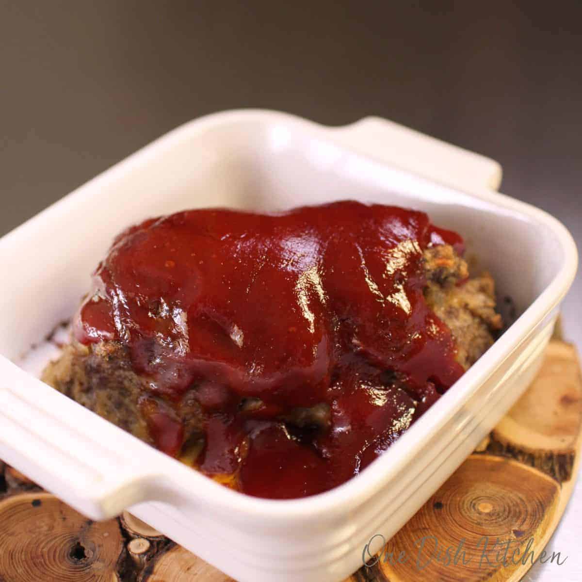 Meatloaf topped with sauce in a small baking dish on a wooden trivet