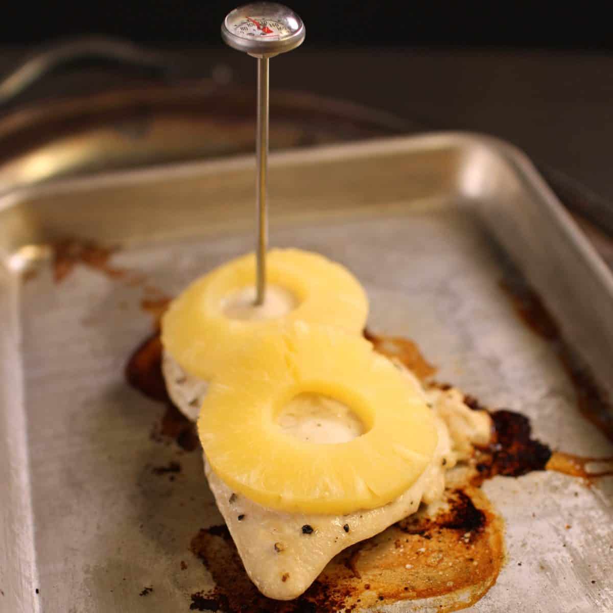 a food thermometer inserted into a chicken breast on a baking sheet.