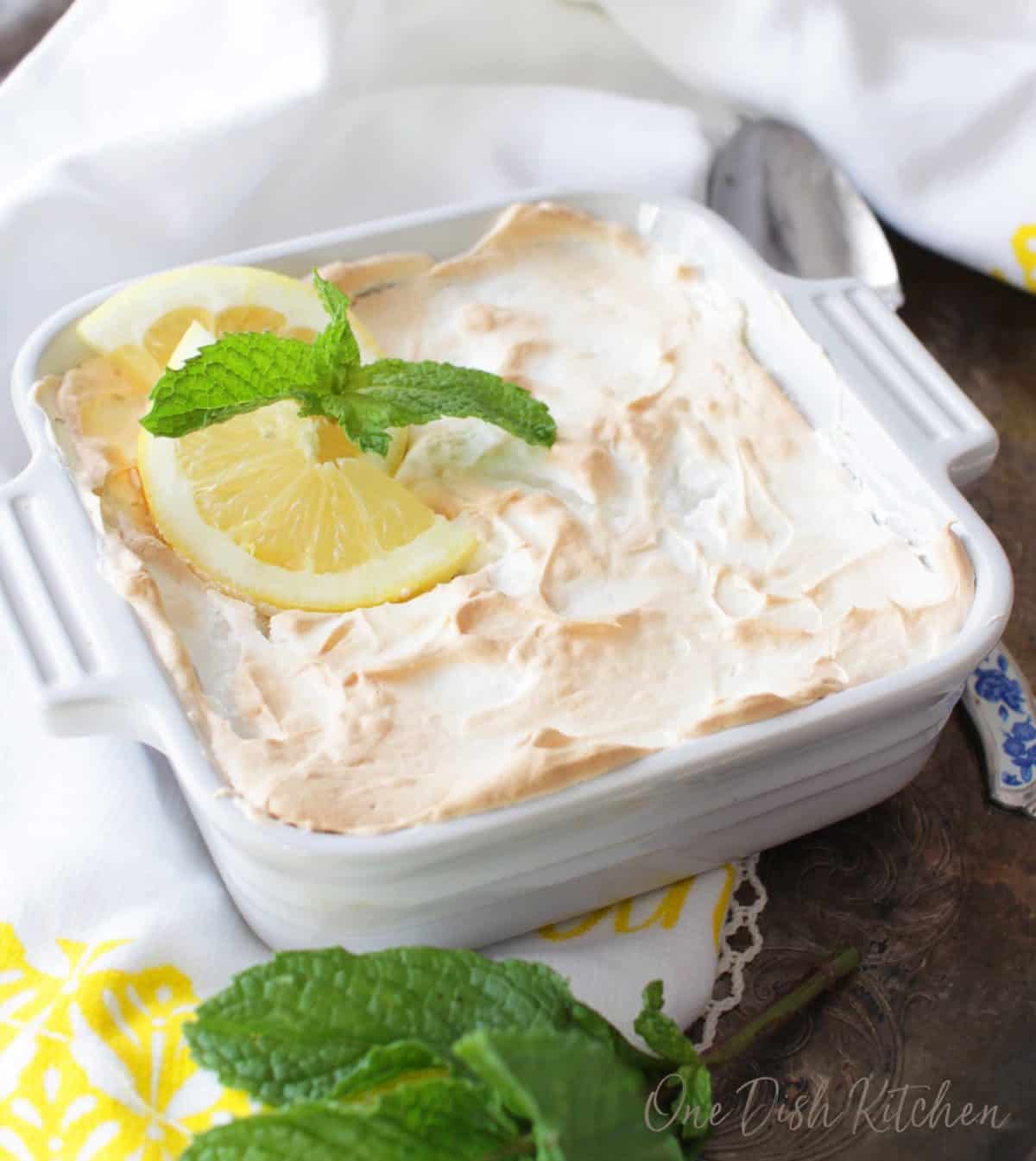 A mini lemon pie garnished with lemon slices and a sprig of fresh mint on a tray next to a yellow and white dish towel.