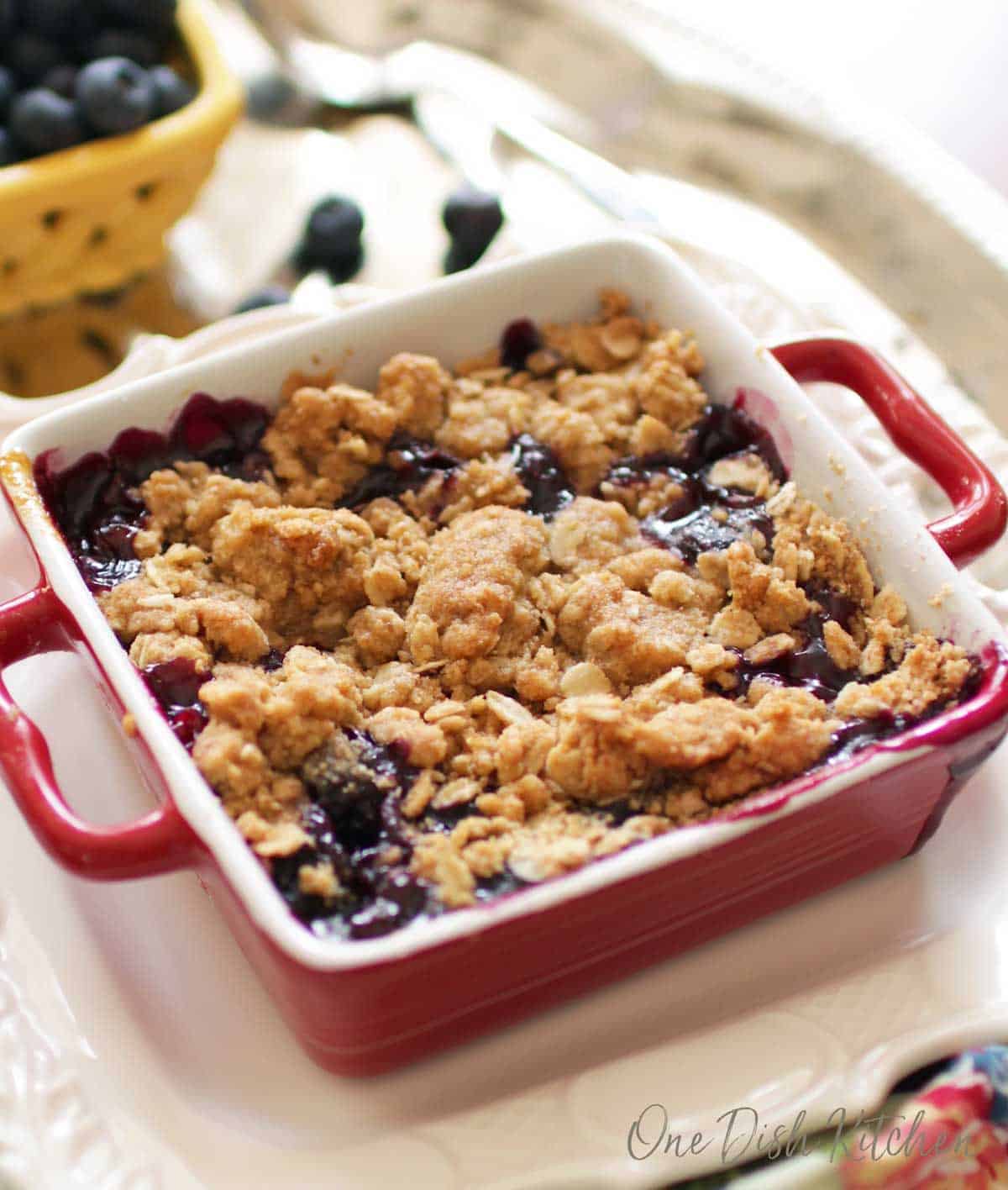 Blueberry crumble in a small red baking dish topped with baked oat topping