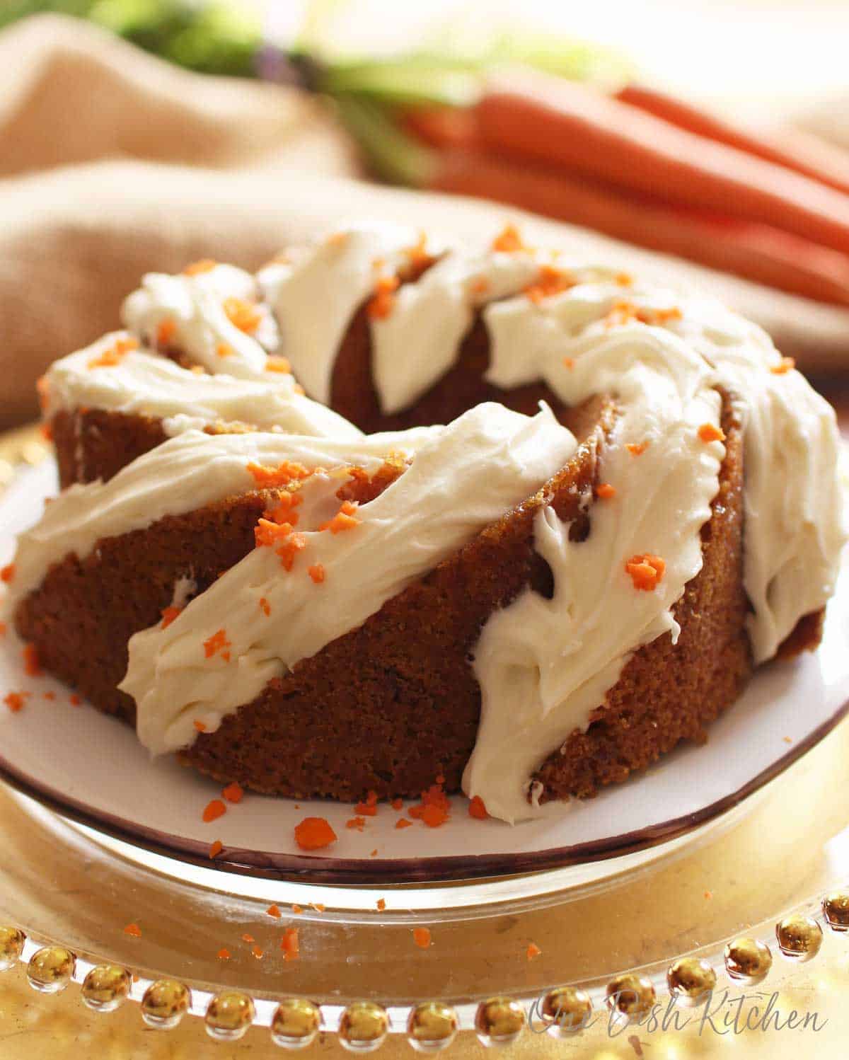 A frosted carrot bundt cake with bits of chopped carrots on top