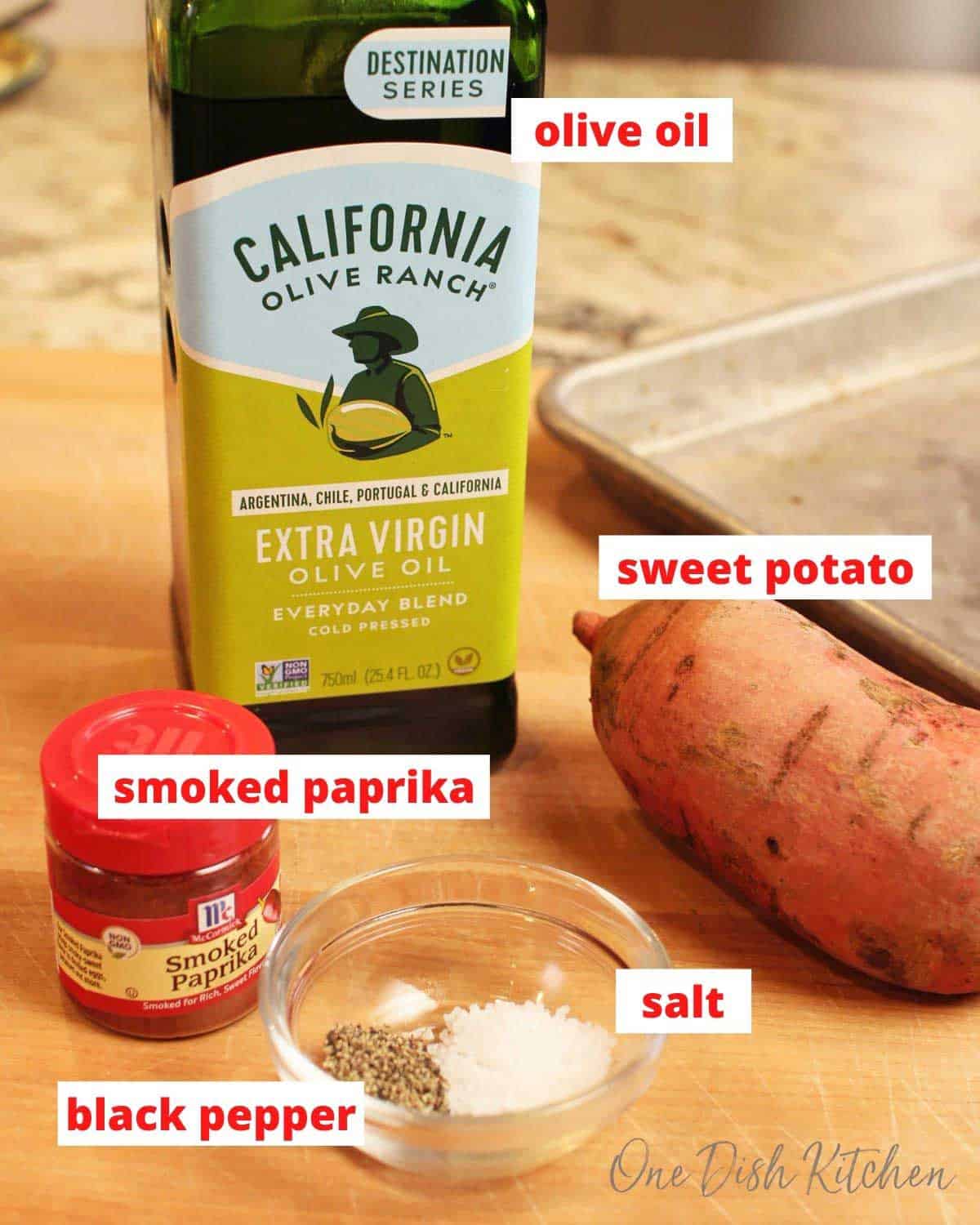olive oil, a sweet potato, spice jar, salt and pepper on a brown cutting board