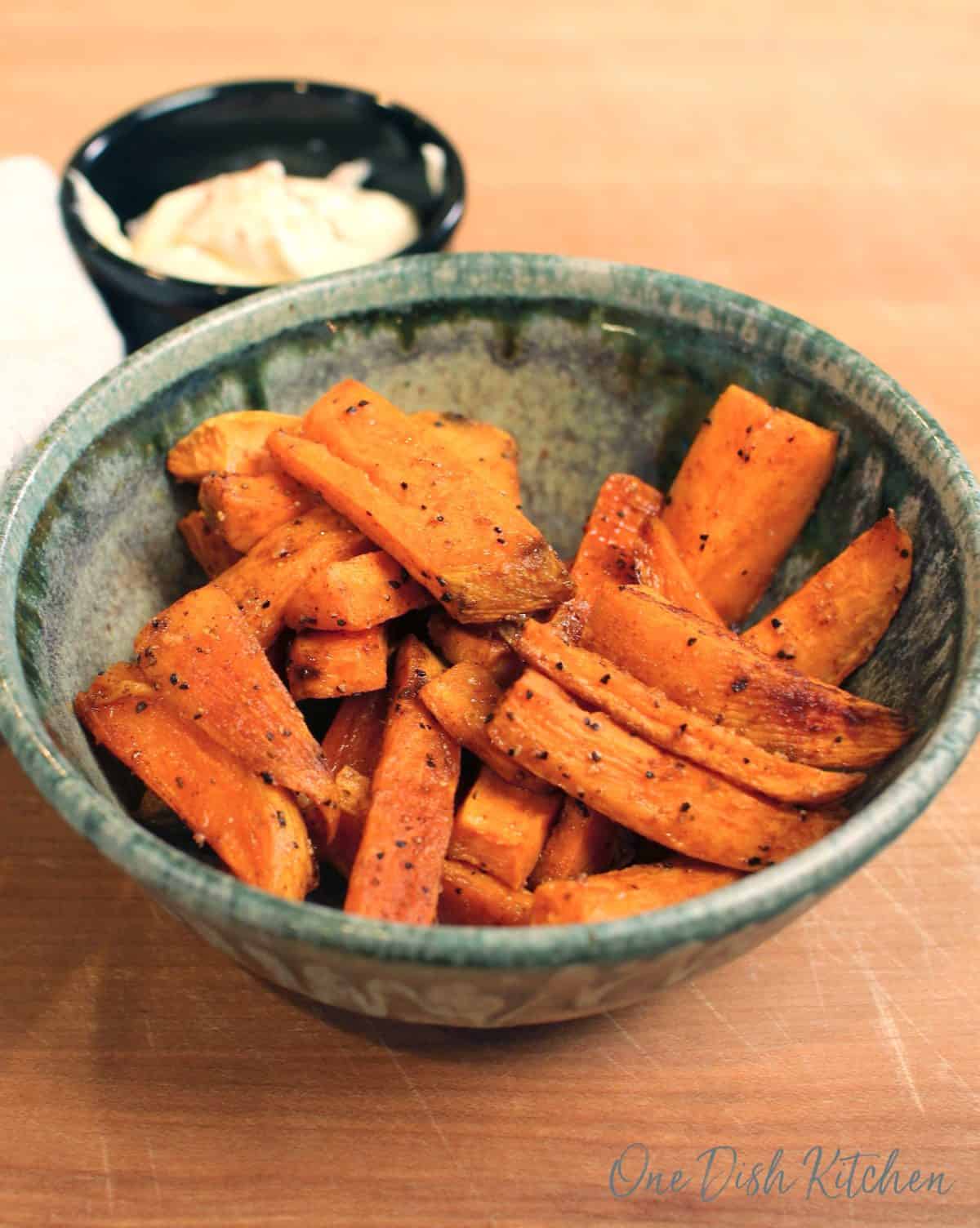 a green bowl filled with sweet potato fries on a brown wood table