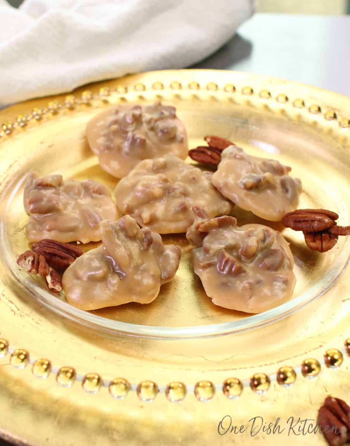 A gold plate with five pecan pralines on it.