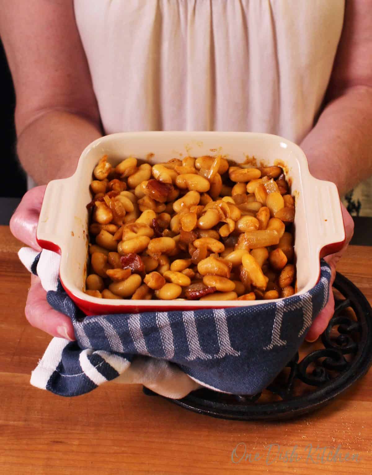 A girl holding and presenting a small baking dish filled with baked beans and bacon.