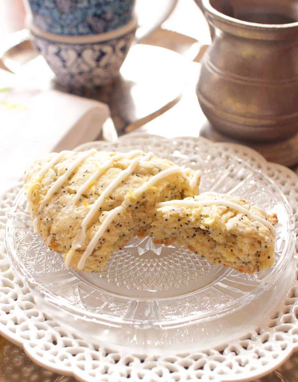A scone topped with white glaze cut in half on a white plate next to a cup of tea.