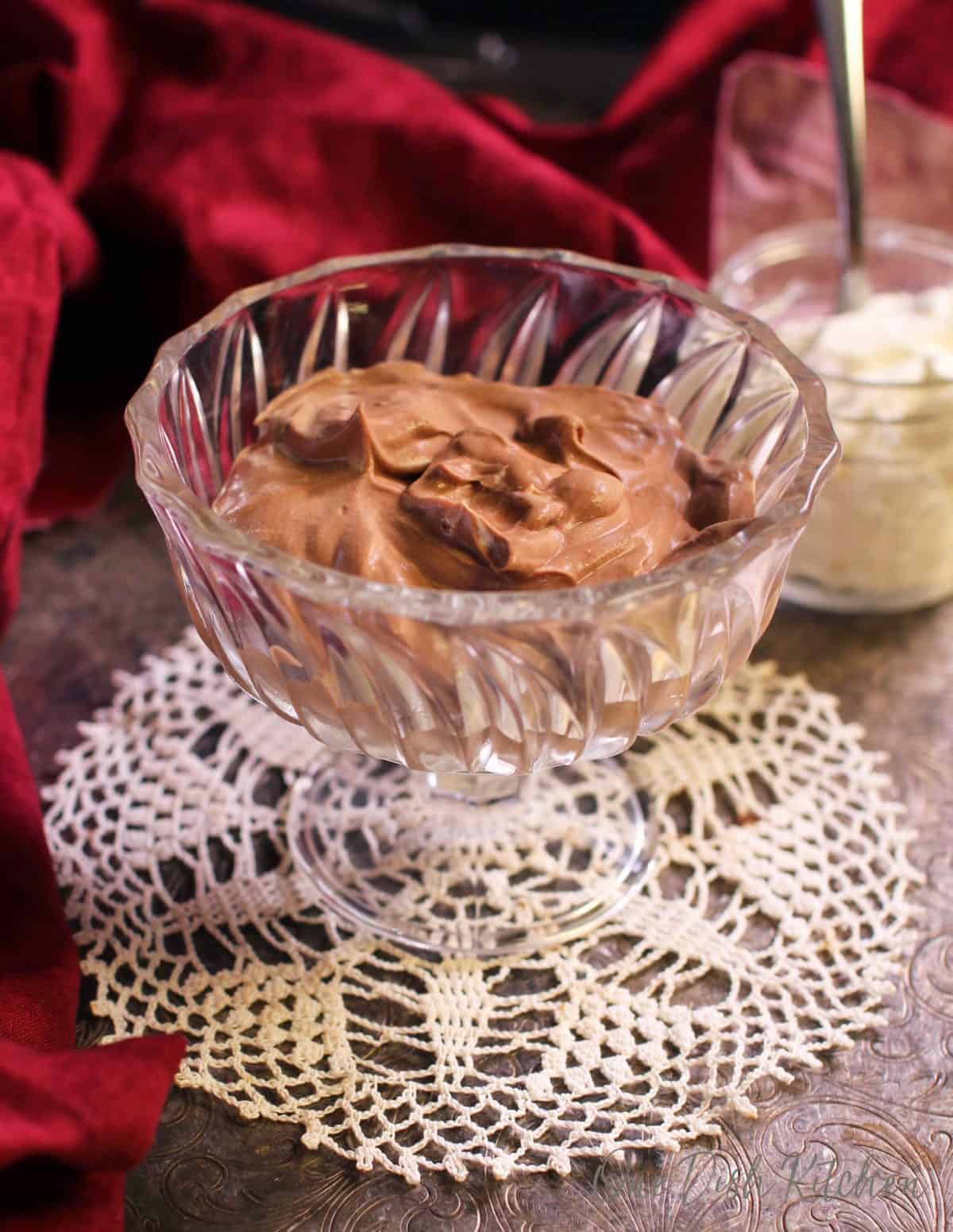 Chocolate mousse in a dessert glass next to a jar of whipped cream and a red cloth napkin all on a metal tray