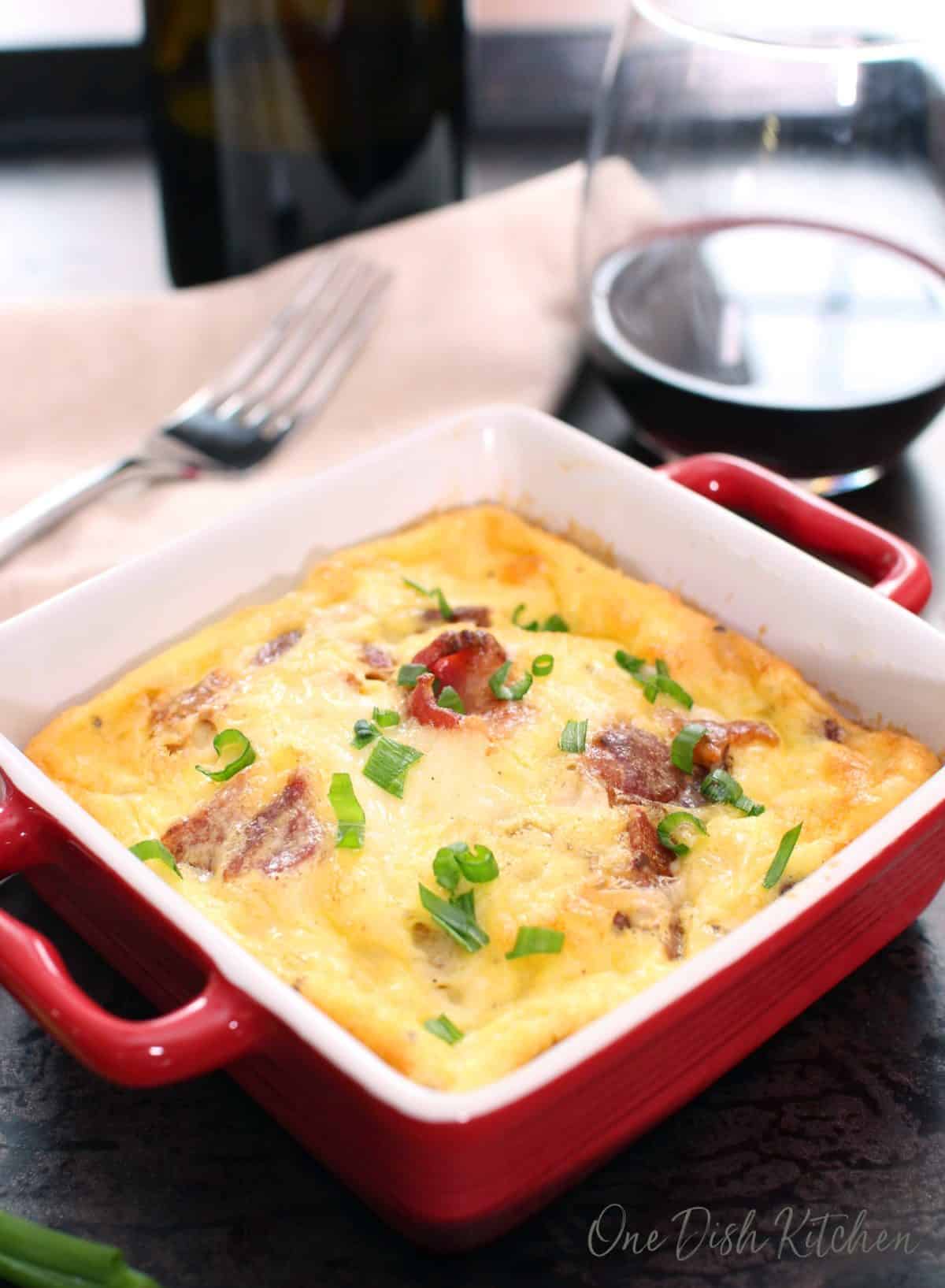 Crustless quiche lorraine baked in a small baking dish on a tray with a glass of red wine