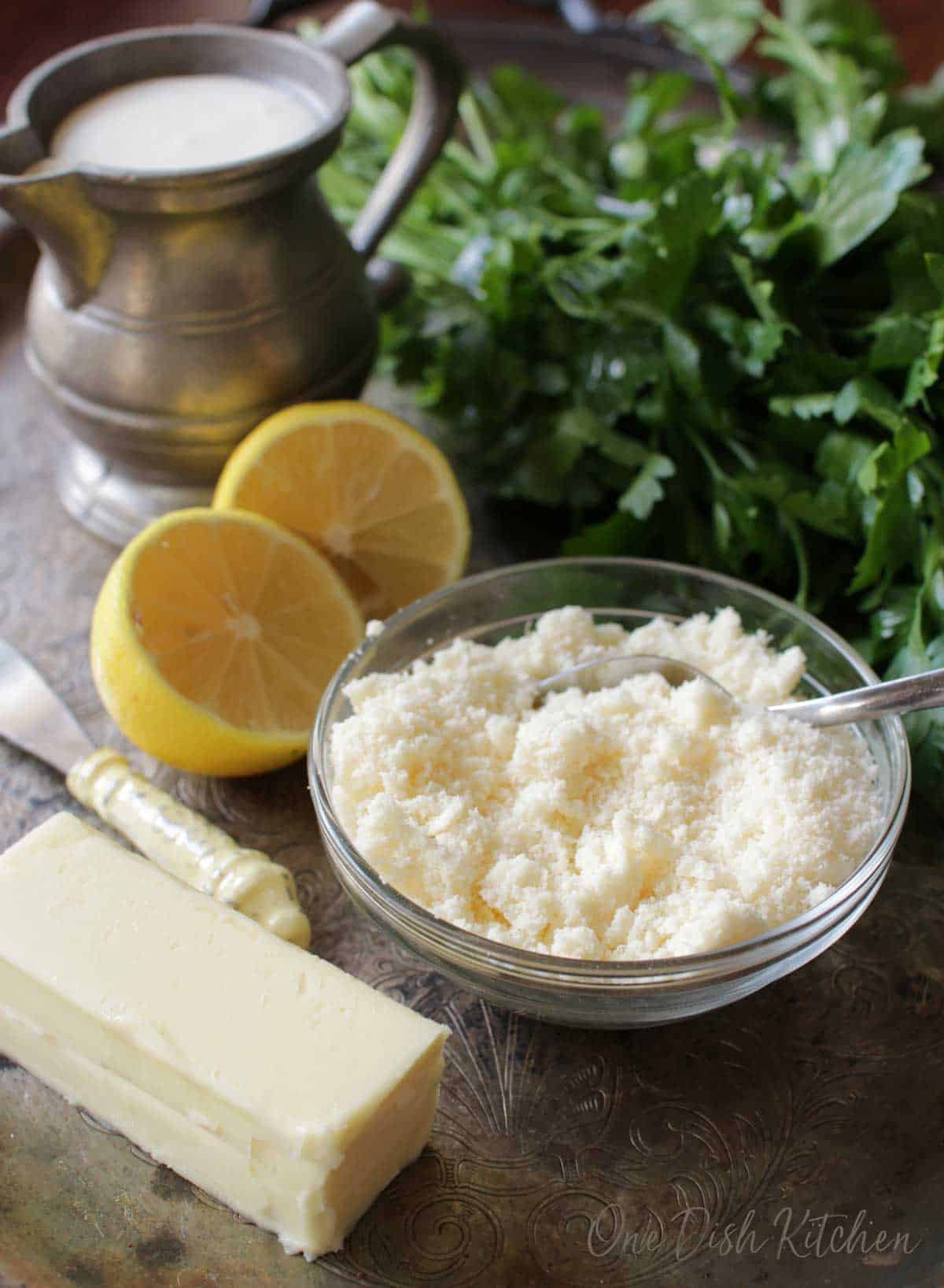 Ingredients for homemade alfredo sauce- cream, lemon halves, a stick of butter, and a small bowl of parmesan cheese all on a metal tray